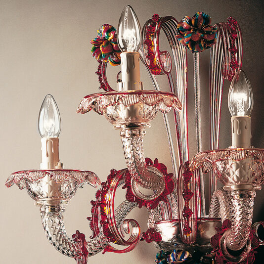 Classic Glass Wall Light With Red Floral Detailing A close-up of an ornate chandelier featuring intricately designed pink and clear glass arms, adorned with colorful floral accents. Reminiscent of the Classic Glass Wall Light With Red Floral Detailing, the chandelier has multiple lit bulbs casting a warm glow.