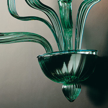 Classic Green Glass Ribbed Detail Wall Light The Classic Green Glass Ribbed Detail Wall Light features a sleek, modern design with curved, elongated glass arms emerging from a central bowl-like base, casting artistic shadows. The intricately crafted ribbed detail on the smooth, glossy finish adds an elegant touch.