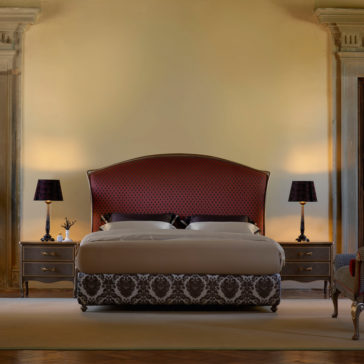 Classic Italian Bed A luxurious bedroom showcases the Classic Italian Bed, adorned with a plush, red and black patterned headboard and an ornate black and white bedspread. Flanking the bed are two wooden nightstands each topped with sleek black lamps. The room exudes elegance with its soft lighting and refined decor.