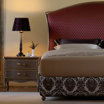 Classic Italian Bed A cozy bedroom showcasing the Classic Italian Bed adorned with patterned bedding and an ornate headboard. Beside the bed, a nightstand holds a decorative lamp and small personal items. Warm ambient lighting enhances the relaxing atmosphere, complemented by walls painted in a soft, neutral shade.