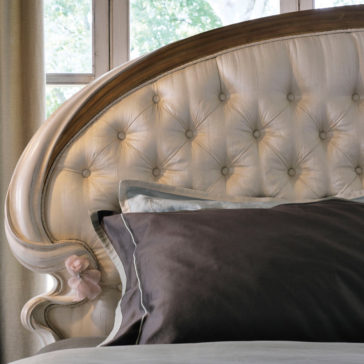 Classic Style Button Upholstered Bed A close-up view of the Classic Style Button Upholstered Bed in a bedroom. The tufted, fabric-covered headboard features intricate button detailing and curved wood trim. Pillows, including a dark gray one in the foreground, adorn the bed. A window with trees visible is in the background.
