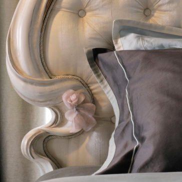 Classic Style Button Upholstered Bed A close-up view of the Classic Style Button Upholstered Bed highlights its elegant white-painted headboard with tufted detailing and button upholstery. A pink decorative flower adorns the headboard, while gray and light-colored pillows are neatly arranged on the bed, complemented by a light curtain in the background.