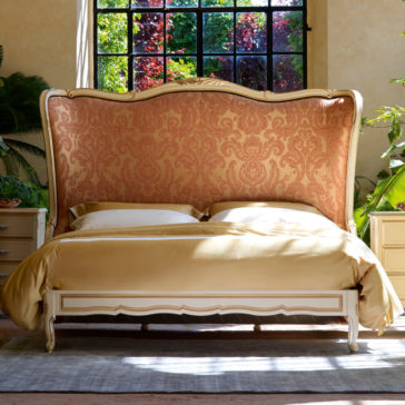 Luxurious bedroom with the Classic Style Tall Winged Bed featuring an ornate, vintage-style headboard upholstered in patterned fabric. The classic-style bed boasts gold bedding, flanked by nightstands on either side. A large window with natural light and lush greenery graces the background.