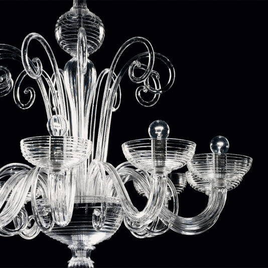 Classic Swirl Detail Glass Chandelier A close-up of the Classic Swirl Detail Glass Chandelier against a black background. The ornate chandelier showcases intricate, swirling and looping designs with multiple arms extending outward, each holding a light bulb encased in a clear glass socket. The glass is clear and glossy.