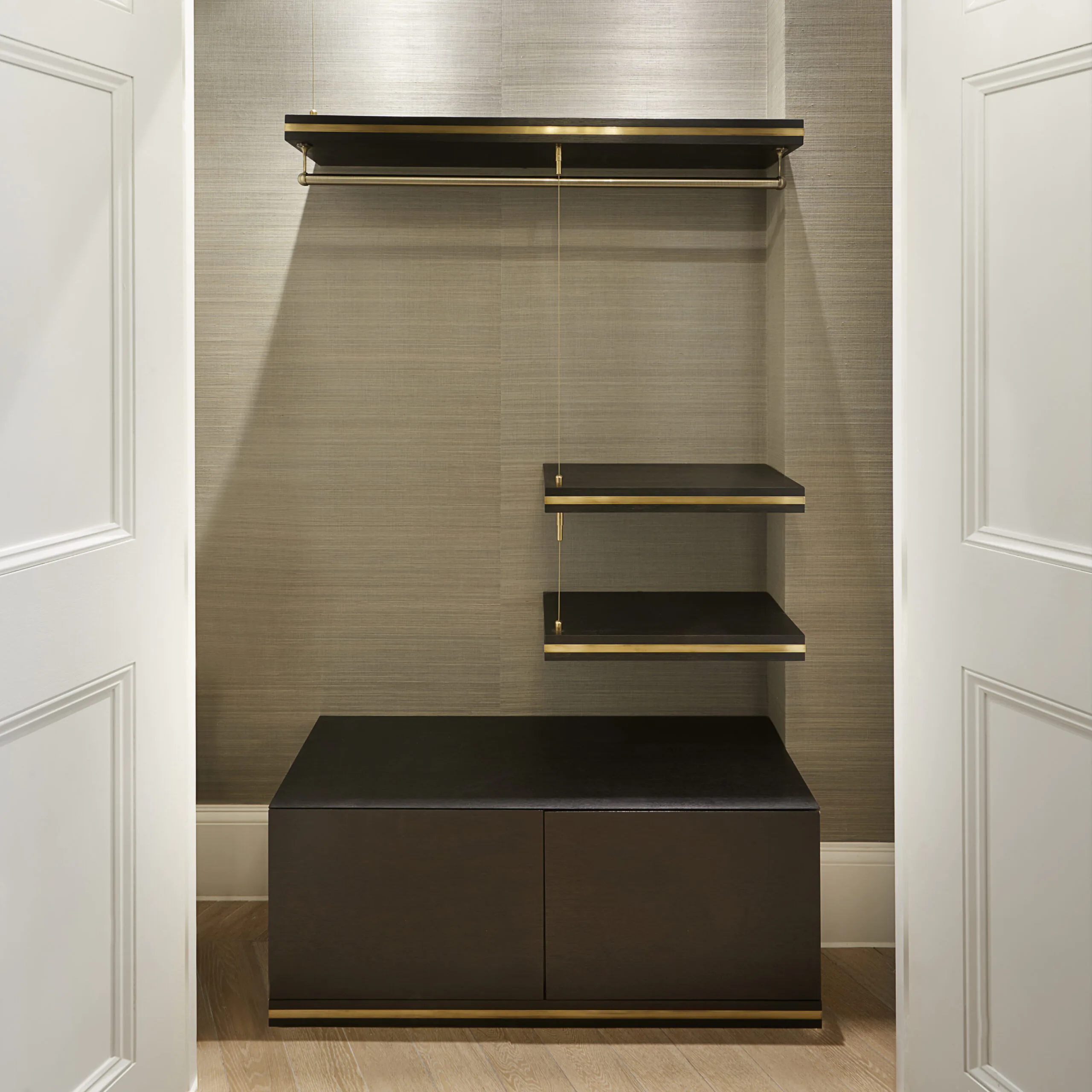 A minimalist closet features a sleek design with a hanging rod, an upper shelf, and three side shelves. Below is a dark wooden storage cabinet. The closet has a light gray textured background and is framed by white doors.