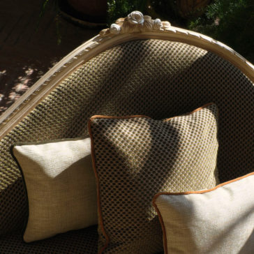 Large Classic Louis Style Chaise Longue In a sunlit room, there is a close-up of the Large Classic Louis Style Chaise Longue adorned with plush cushions. The chaise boasts an ornately carved crest, while the cushions display complementary geometric designs in earth tones, imparting a cozy and sophisticated ambiance.