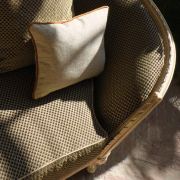 Large Classic Louis Style Chaise Longue A Large Classic Louis Style Chaise Longue with a small diamond pattern is displayed in partial sunlight. A square cream-colored throw pillow with brown piping accents the chair. Sunlight filters through, casting dappled shadows on the arm and seat, bringing out its rich textures.
