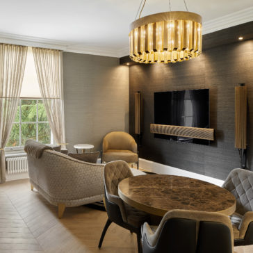 Luxurious Round Designer Chandelier A modern living room featuring a black accent wall with a mounted flat-screen TV and speakers. A marble dining table with upholstered chairs sits under the Luxurious Round Designer Chandelier. Light gray sofas and a large window with beige curtains complete the elegant design.