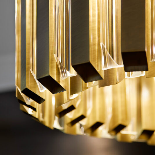 The Luxurious Round Designer Chandelier offers a captivating close-up view of its sleek, modern design. This elegant lighting fixture showcases multiple rectangular gold frames paired with clear glass sections, each elegantly holding lightbulbs. When illuminated, the chandelier emits a warm, reflective glow that enhances its surroundings, with the background tastefully out of focus.