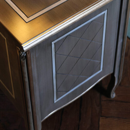 Luxury Italian Bedside Cabinet Close-up of the Luxury Italian Bedside Cabinet corner, showcasing its intricate geometric carvings. The front panel is adorned with a raised diamond pattern, while the top features a lighter wood inlay border. Standing on delicately curved legs, this cabinet exemplifies fine craftsmanship and elegant design.