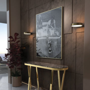 A modern hallway showcases a vertical black-and-white framed photograph on a wooden wall, flanked by two circular wall lights. Below, a Luxury Premium Marble Console Table with gold legs holds decorative items. A potted plant is placed beside the table, adding a touch of greenery to the premium space.