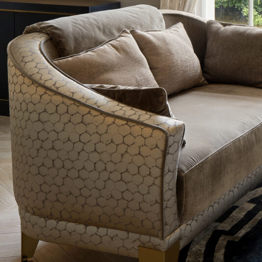 Luxury Small Two-Tone Sofa The Luxury Small Two-Tone Sofa features an elegant hexagonal pattern on its armrest, soft beige upholstery, and several plump two-tone cushions. Positioned near a window, the sofa allows natural light to highlight its plush fabric and intricate design.
