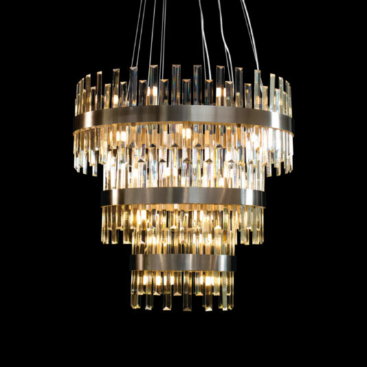 The Modern Crystal Three Tier Chandelier, featuring several concentric metal rings adorned with vertical crystal prisms, hangs against a black background. Warm white lights shine from within its luxurious, modern design, creating a radiant and elegant ambiance.