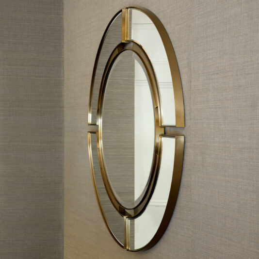 Mounted on a beige textured wall is the Modern Designer Round Mirror, featuring a sleek gold frame that divides the mirror into four curved segments, creating a stylish and contemporary design.