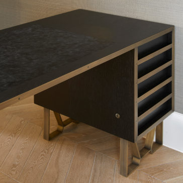 Modern Industrial Style Oak Veneer Desk A sleek Modern Industrial Style Oak Veneer Desk with a minimalist design placed against a grey wall. The desk features angled metal legs and a drawer unit with multiple open slots on the right side. The surface has a dark, textured area resembling a desktop mat. The wooden floor enhances its oak veneer finish.