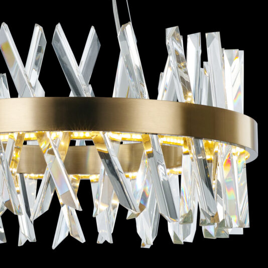 Round Crystal And Brass Chandelier A close-up of the Round Crystal And Brass Chandelier showcasing its circular gold frame adorned with crisscrossing clear crystal elements. The chandelier is illuminated, casting a warm glow that reflects off the crystals and creates a sparkling effect against a black background.