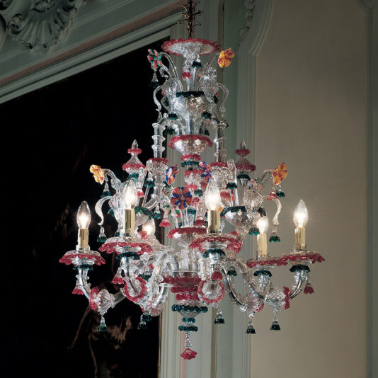 The Statement Chandelier With Colourful Floral Detailing, featuring six candle-shaped light bulbs and adorned with multicolored glass decorations, hangs in an elegant room with detailed molding on the walls. Its intricate and vibrant floral design adds a touch of sophistication to the space.