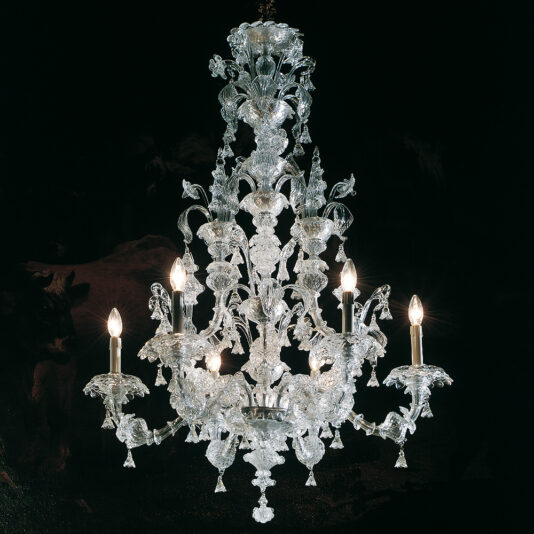The Traditional Clear Glass Chandelier, an ornate multi-tiered fixture, is illuminated by several candle-like bulbs against a dark background. It features intricate glasswork adorned with floral and leaf motifs, enhancing its luxurious and elegant appearance.