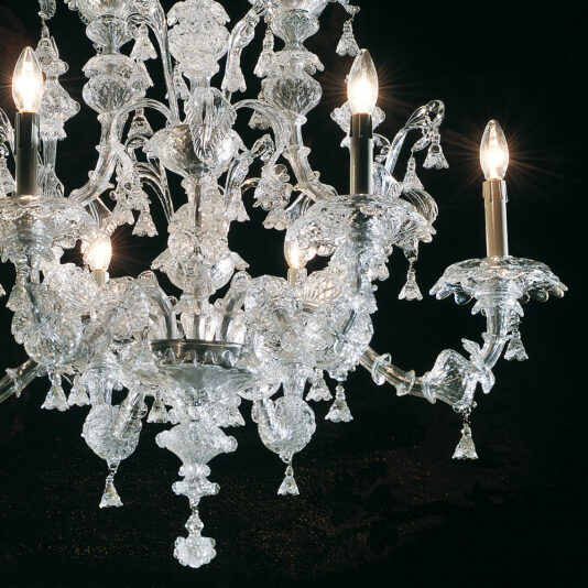 Traditional Clear Glass Chandelier The Traditional Clear Glass Chandelier, with its intricately detailed glasswork and multiple arms adorned with candle-like light bulbs, shines beautifully against a dark background. Its prisms refract light to create a sparkling effect.