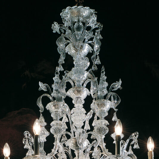 Traditional Clear Glass Chandelier A detailed Traditional Clear Glass Chandelier with intricate designs hangs against a dark background. The chandelier, made of clear glass, features multiple ornate crystal elements with several candle-shaped light bulbs evenly distributed around the structure.