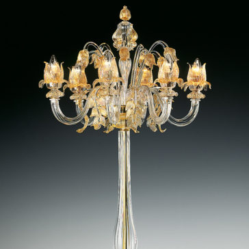 Classic Floral Gold Glass Floor Lamp The Classic Floral Gold Glass Floor Lamp stands tall and elegant with eight intricately designed, curved glass arms that extend outwards, each holding a candle-like light encased in floral-shaped glass. The classic fixture casts a golden glow against a dark background when illuminated.