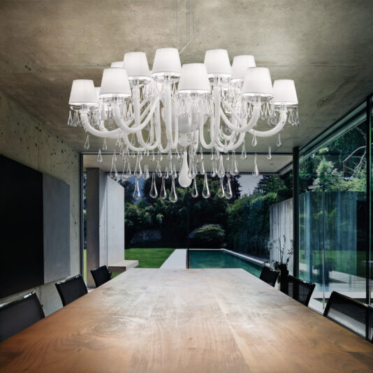 Classic Glass Teardrop Accent Chandelier A modern dining room features a long wooden table surrounded by black chairs. The space is illuminated by the Classic Glass Teardrop Accent Chandelier, an elegant fixture with multiple lampshades and hanging crystal drops. Large glass windows provide a stunning view of the lush garden and swimming pool outside.