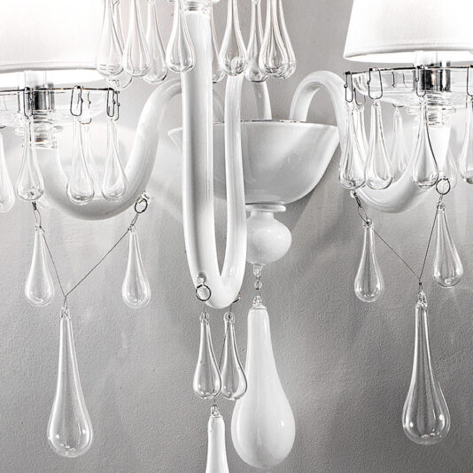 Classic Glass Teardrop Accent Wall Light With Three Arms Close-up of the Classic Glass Teardrop Accent Wall Light With Three Arms, a stylish, white wall-mounted chandelier adorned with intricate glass ornamentation. This elegant fixture features clear, drop-shaped glass pendants hanging delicately from curved arms, softly reflecting light against a white background.