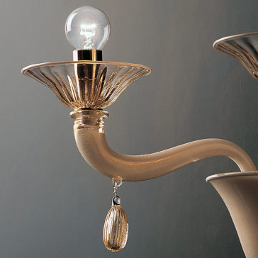 Classic Gold Glass Wall Light With Gold Frame A close-up of the Classic Gold Glass Wall Light With Gold Frame, featuring a vintage-style design with a curved beige arm, a translucent decorative sconce, and a clear light bulb. Below the sconce hangs a small ornamental charm. The background is a gradient of light to dark gray.