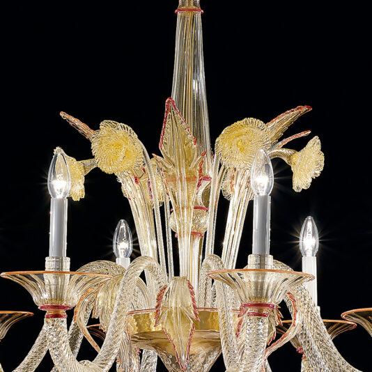 Classic Ornate Gold And Red Glass Chandelier A close-up view of the Classic Ornate Gold And Red Glass Chandelier reveals its elegant design, featuring intricate patterns that resemble flowers and leaves. This exquisite piece includes multiple candle-like light bulbs that emit a soft glow, with glass accents in rich red and gold hues against a black background.