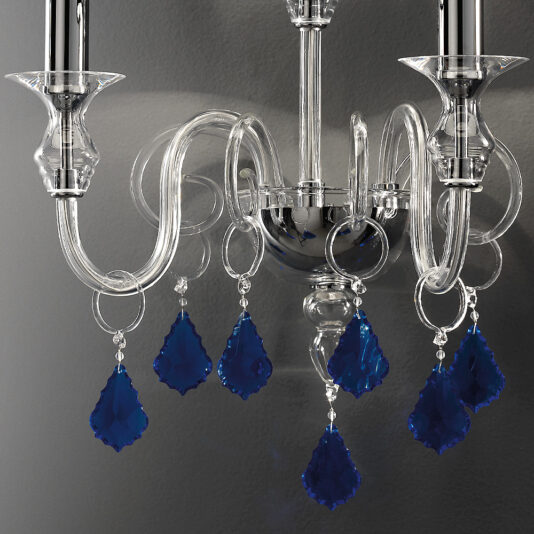Classic Wall Light With Blue Crystal Drops A close-up of the Classic Wall Light With Blue Crystal Drops showcases its elegant, curved glass arms. Several teardrop-shaped blue glass pendants hang from the chandelier, adding a vibrant pop of color. The intricate details are highlighted against a dark, matte wall background.