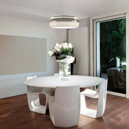 Contemporary Dome Glass Pendant Light A modern dining room features a round white table surrounded by four contemporary white chairs, all set atop a wooden floor. A vase filled with white flowers sits elegantly on the table. Overhead, the sleek Contemporary Dome Glass Pendant Light hangs gracefully, illuminating the space. A large window provides an inviting view of the garden outside.