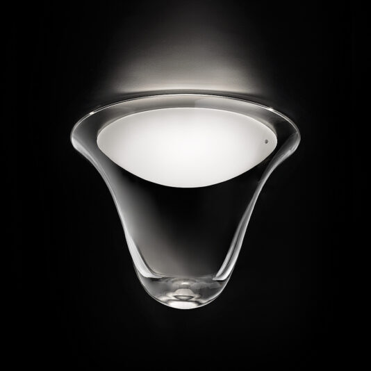 A modern, cone-shaped wall sconce with a smooth, white inner surface emits a soft, ambient light upwards. Reminiscent of the Contemporary Frosted Glass Ceiling Light, the fixture is set against a dark background, highlighting its sleek, glossy design and gentle curves.