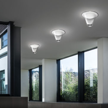 A modern hallway with large windows on one side, allowing natural light to illuminate the space. The ceiling features three **Contemporary Frosted Glass Ceiling Lights**. Outside the windows, greenery and foliage are visible.