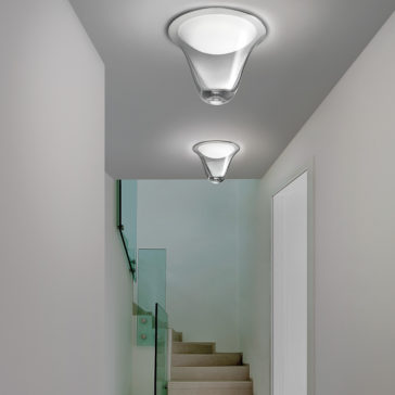 A minimalist hallway features two Contemporary Frosted Glass Ceiling Lights. At the end, a short flight of light-colored wooden stairs with a glass railing leads to an upper level. The walls are painted white, enhancing the clean and contemporary design.