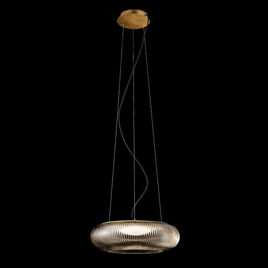 The Contemporary Ribbed Glass Pendant Light With Gold Frame hangs from the ceiling on three wires, featuring a brass-colored canopy and suspended cables. The fixture illuminates from within its textured glass, casting a warm glow against the solid black background.