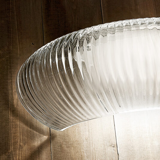 Contemporary Ribbed Glass Wall Light A close-up of the Contemporary Ribbed Glass Wall Light, featuring intricate detailing, illuminated and casting subtle shadows on a wooden ceiling.