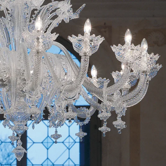 Deluxe Floral Clear Glass Chandelier The Deluxe Floral Clear Glass Chandelier features intricate floral-inspired glasswork with twisting arms and candle-shaped bulbs. A patterned window in the background softly diffuses natural light into the room.
