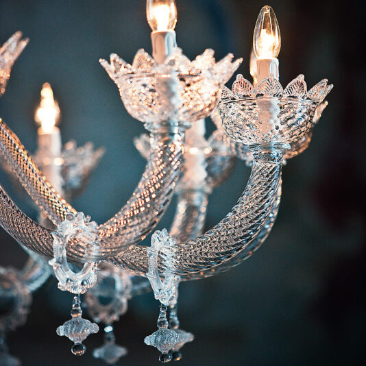 Deluxe Floral Clear Glass Chandelier A close-up shot of the Deluxe Floral Clear Glass Chandelier, showcasing its luxurious and classic design with ornate details and multiple light bulbs. This clear glass chandelier features intricate glasswork and decorative floral elements, glowing warmly to create a sense of elegance and sophistication.