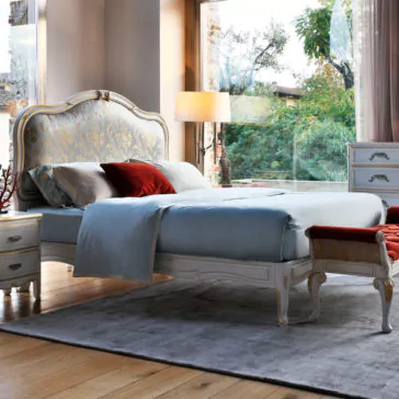 Elegant Classic Style Bed Luxurious bedroom showcasing the Elegant Classic Style Bed, a king-sized masterpiece featuring an ornate headboard. The bed is dressed in pale blue bedding and accented with a red pillow. The room boasts wooden floors, sophisticated furniture, floor-to-ceiling windows, and a view of the garden. A soft area rug lies beneath the bed for added comfort.
