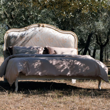 Elegant Classic Style Bed The Elegant Classic Style Bed, featuring an ornate headboard and enveloped in soft bedding, is placed outdoors under trees casting dappled shadows. With light, neutral-colored sheets and pillows, the bed blends beautifully with the natural surroundings.