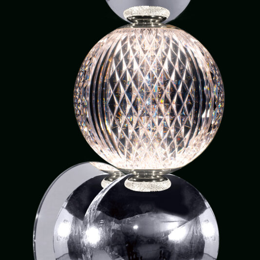 Luxury Chrome Crystal Wall Light Close-up of a polished, spherical crystal light fixture with intricate diamond-shaped patterns. The light shines through, creating a prismatic effect. Below it, a reflective silver sphere adds to the modern and elegant aesthetic. Background is black.