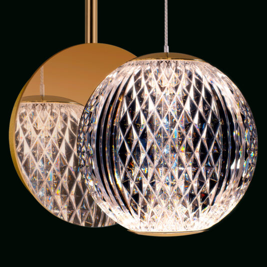 Exclusive Crystal Ball Wall Light A spherical, diamond-patterned crystal pendant light hangs in front of a glossy, gold-colored disc. The light reflects and refracts, creating a brilliant, sparkling effect against the dark background.