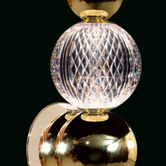 Exclusive Gold Crystal Wall Light A close-up of an elegant table lamp featuring a polished gold base and a spherical glass centerpiece with a diamond-patterned texture, emitting a bright, radiant light.