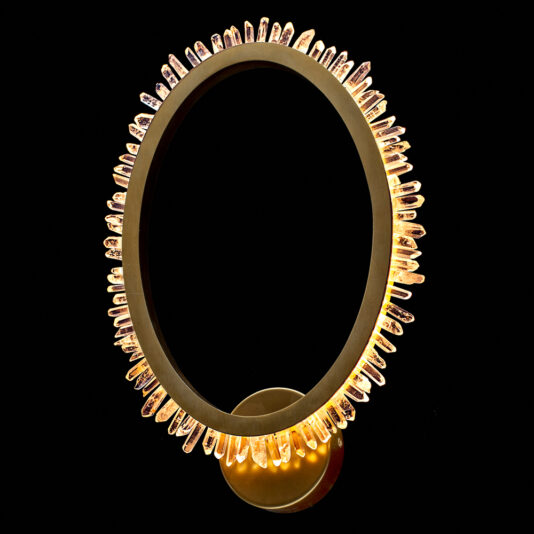 A modern, circular light fixture featuring a ring adorned with exclusive quartz crystal elements that emit a warm, golden glow, the Exclusive Quartz Crystal Gold Wall Light is mounted on a simple, round base against a black background.