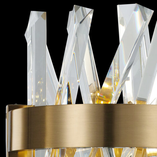 Close-up view of the Exclusive Crystal Brass Wall Light, showcasing a circular brushed gold metal frame adorned with multiple clear crystal prisms pointing upwards. It casts beautiful reflections and exudes a luxurious, elegant aesthetic against a solid black background.