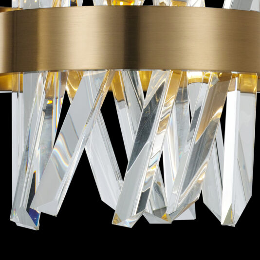 A detailed look at the Exclusive Crystal Brass Wall Light reveals a magnificent chandelier with angled, crystal-like glass pieces and a polished brass circular frame. When illuminated, it casts a warm glow and reflects beautifully off the glass elements, showcasing the elegance of this high-end fixture.