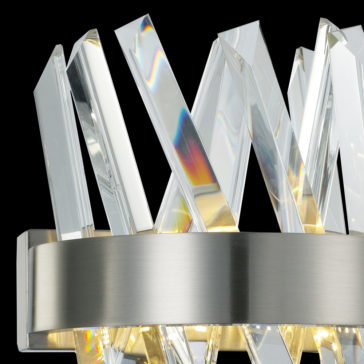 Exclusive Crystal Nickel Wall Light Close-up of the Exclusive Crystal Nickel Wall Light, showcasing its brushed metal base and multiple angled crystal light diffusers. The crystals are arranged in an overlapping V-shaped pattern, casting colorful light reflections. The black background highlights the fixture’s intricate design.
