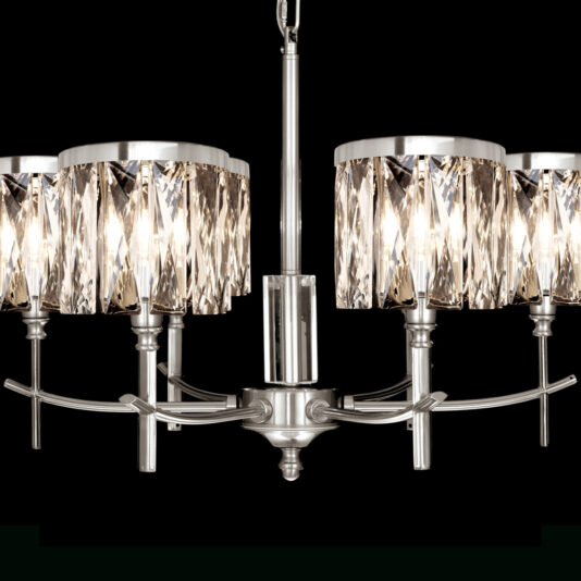 High End 6 Arm Nickel Chandelier A modern chandelier with six cylindrical lampshades made of faceted glass, set in a polished silver metal frame. The chandelier is lit, casting a warm glow through the glass and highlighting its geometric design. The background is solid black.