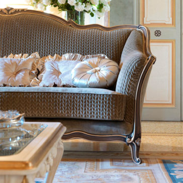 Luxury Venetian Style Sofa Transform your living room into a luxurious retreat with the elegant Luxury Venetian Style Sofa, upholstered in patterned fabric and adorned with silk cushions. This exquisite piece features detailed woodwork that adds a touch of opulence. Complementing the sofa is a beautifully designed glass coffee table and a plush rug, while a bouquet of flowers adds a fresh touch to the background.