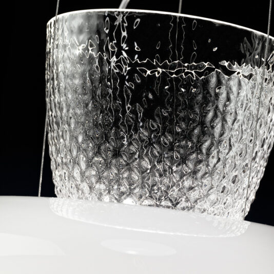 Modern Glass Dome Pendant Light Close-up of the Modern Glass Dome Pendant Light, showcasing its textured, translucent glass dome illuminated from within. The pendant light hangs on thin wires against a black background, with the glass exhibiting a pattern that evokes rippling water or frost. The bottom part of the lampshade is white and opaque.